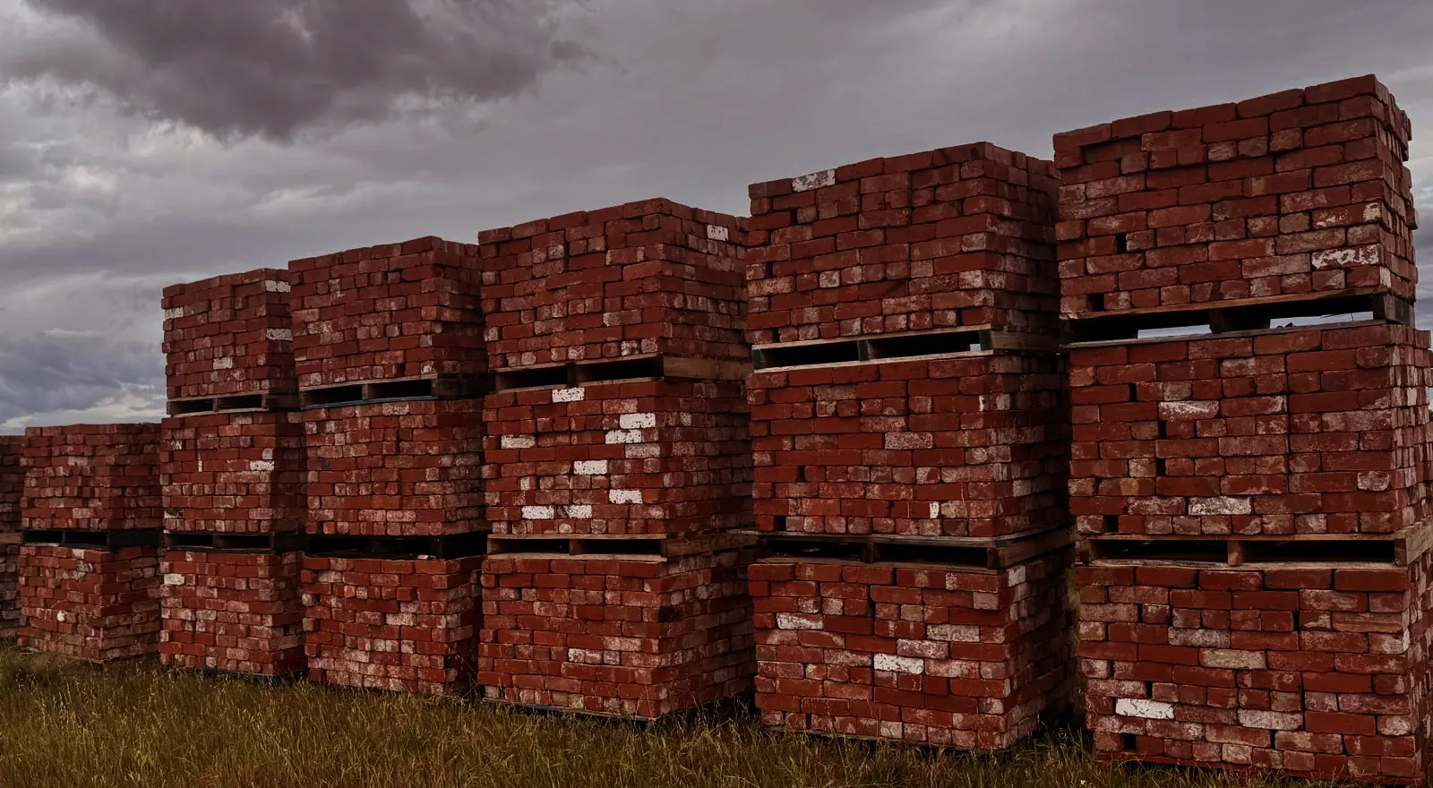 Rows of recycled brick pallets in the Ali Recycled Bricks yard under a stormy sky